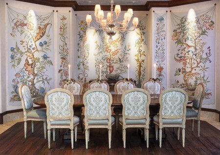 an Intricate, detailed dining room table with custom fabric chairs, ornate wallpaper and lighting.